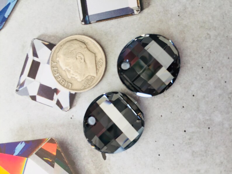 May include: Two black round glass rhinestones with a faceted design. The rhinestones are about 1 inch in diameter.