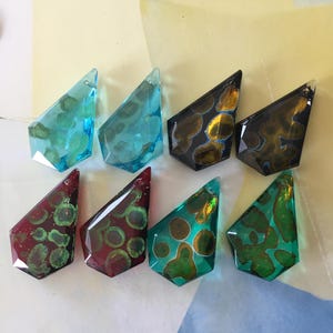 Può includere: Otto ciondoli di vetro in vari colori e motivi. I ciondoli hanno la forma di una lacrima con una punta appuntita. I colori includono blu, verde, rosso e nero. Alcuni dei ciondoli hanno una finitura metallica dorata o argentata.