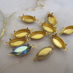 Puede incluir: Un grupo de ocho engastes de metal dorado para piedras en forma de marquesa. Los engastes tienen dos bucles a cada lado para sujetar a las joyas. Un engaste tiene una piedra en forma de marquesa azul iridiscente.