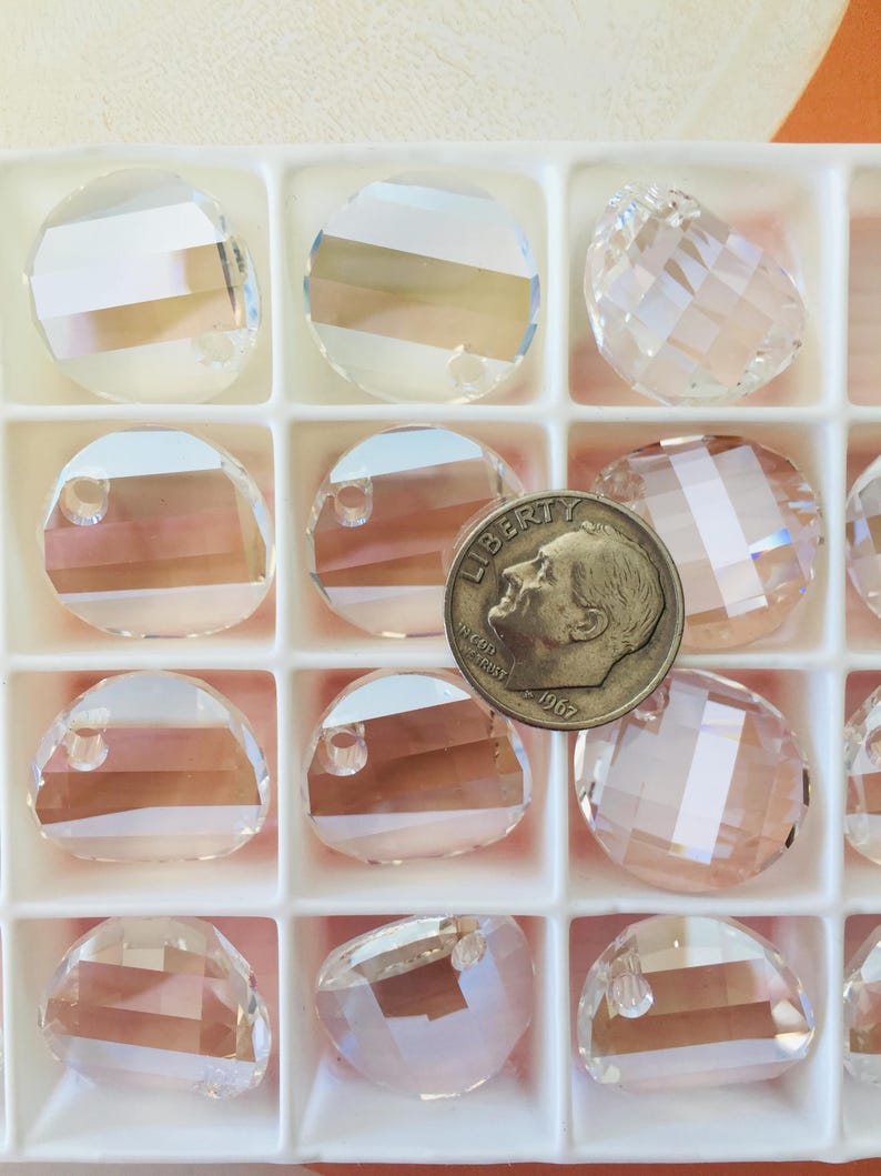 May include: A close-up of a white plastic container filled with clear glass beads. The beads are round and have a hole in the center. A US dime is included for scale.