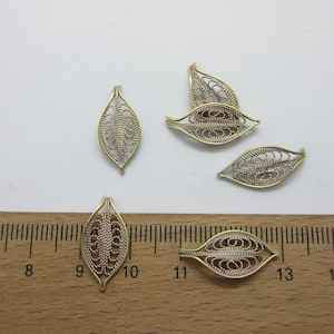 May include: Five gold filigree leaf charms, each with a delicate, intricate design. The charms are approximately 1 inch in length and are shown against a white background with a ruler for scale.