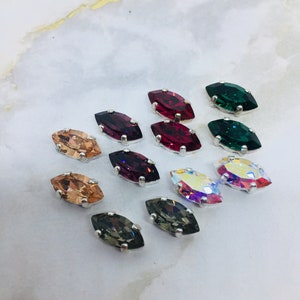 May include: Assortment of marquise-shaped rhinestones in various colours, including green, red, pink, and brown. The rhinestones are set in silver settings.