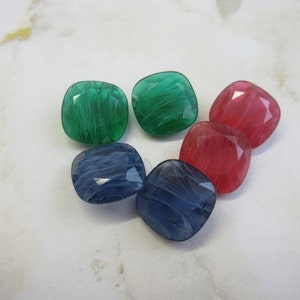 May include: Six square-shaped buttons with a swirled pattern. Two are green, two are blue, and two are pink.