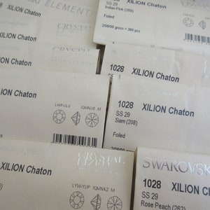 Op de afbeelding: Close-up van verschillende kleine witte kaartjes met de tekst "XILION Chaton" en verschillende kleurennamen en nummers. De kaartjes zijn gelabeld met "SS 29" en hebben een klein afbeelding van een kristal op elk kaartje.