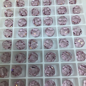 May include: A close-up view of a container filled with small, round, light pink glass beads. The beads are arranged in a grid pattern and have a faceted design.