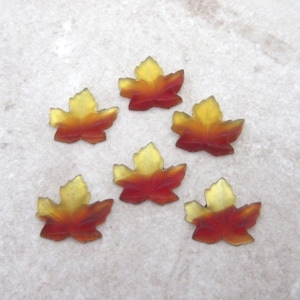 May include: Six small maple leaf-shaped embellishments made of translucent material. Each piece features a gradient color transition from a deep reddish-orange at the base to a bright yellow at the top, mimicking the appearance of autumn foliage.