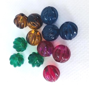 Puede incluir: Una colección de cuentas de vidrio redondas y coloridas. Las cuentas son en tonos ámbar, marrón, verde, azul y rojo. Cada cuenta tiene una textura acanalada y un agujero para ensartar. Ideal para hacer joyas o proyectos de manualidades.