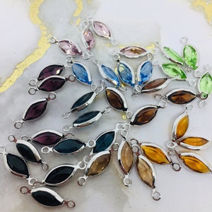 May include: Assortment of colorful crystal connectors with silver-toned metal loops. The connectors are shaped like marquise-cut gemstones and come in shades of green, blue, purple, pink, and brown.