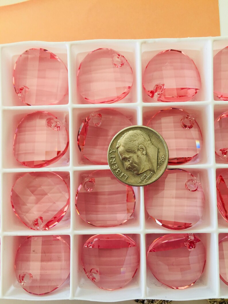 May include: A close-up of a box of pink round crystal beads with a US quarter for scale. The beads have a hole in the top for stringing.