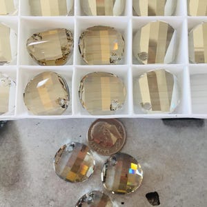 May include: A close-up of a container of round, clear glass beads with a gold iridescent finish. The beads have a hole at the top for stringing. There are four beads outside of the container, next to a US quarter.