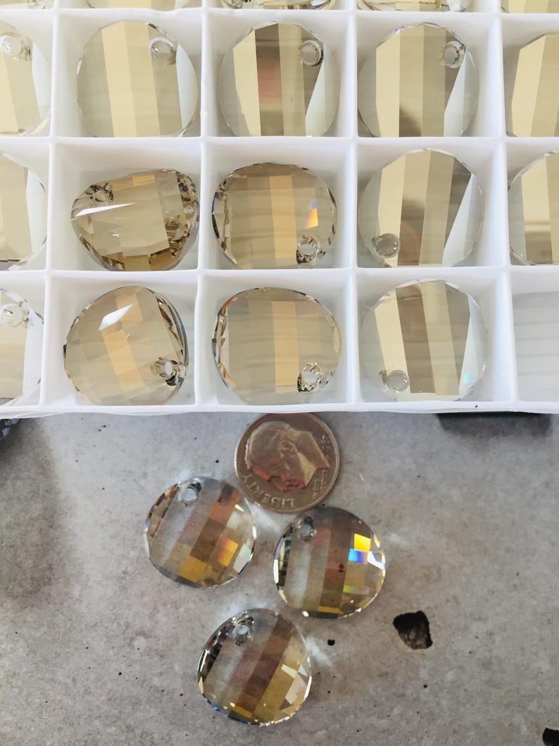 May include: A close-up of a container of round, clear glass beads with a gold iridescent finish. The beads have a hole at the top for stringing. There are four beads outside of the container, next to a US quarter.