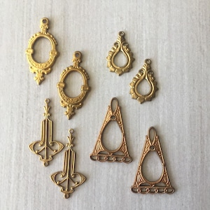 Op de afbeelding: Een verzameling sierlijke metalen bedels in vintage-stijl in goud- en kopertinten. De bedels omvatten ovale, druppel- en geometrische vormen, elk met ingewikkelde filigraan details en kleine lussen.