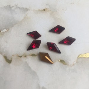 May include: Assortment of red and gold diamond-shaped rhinestones on a white marble background.