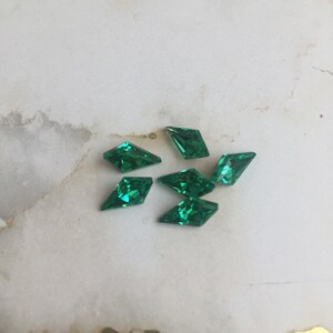 May include: Six green diamond-shaped rhinestones on a white background.