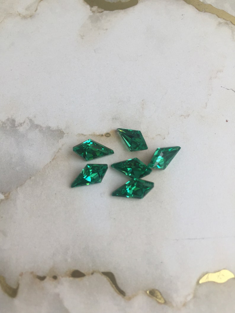 May include: Six green diamond-shaped rhinestones on a white background.