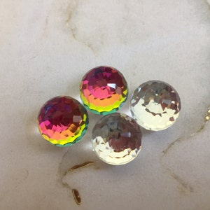 Puede incluir: Cuatro cuentas de vidrio iridiscente, dos son transparentes y dos son multicolores con tonos rosados, naranjas, amarillos y verdes.