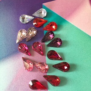 May include: Assortment of teardrop-shaped crystal rhinestones in various shades of red, pink, and clear. The rhinestones are arranged in a gradient pattern, with the darkest shades at the top and the lightest shades at the bottom.