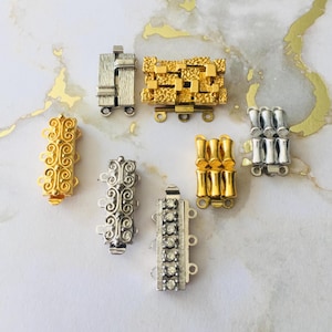 May include: A collection of jewelry clasps in various designs and finishes. The clasps include gold-toned, silver-toned, and rhinestone-studded options. Styles range from ornate filigree to geometric shapes, showcasing a variety of textures and details.