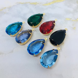 May include: Seven teardrop-shaped glass pendants with gold-toned metal loops. The pendants are in various colors, including green, red, blue, light blue, and black.