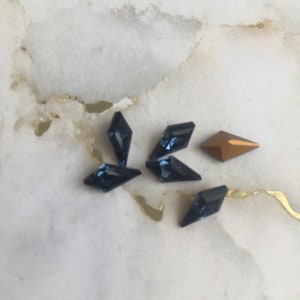 May include: A group of six small, faceted rhinestones. Five are dark blue and one is gold.