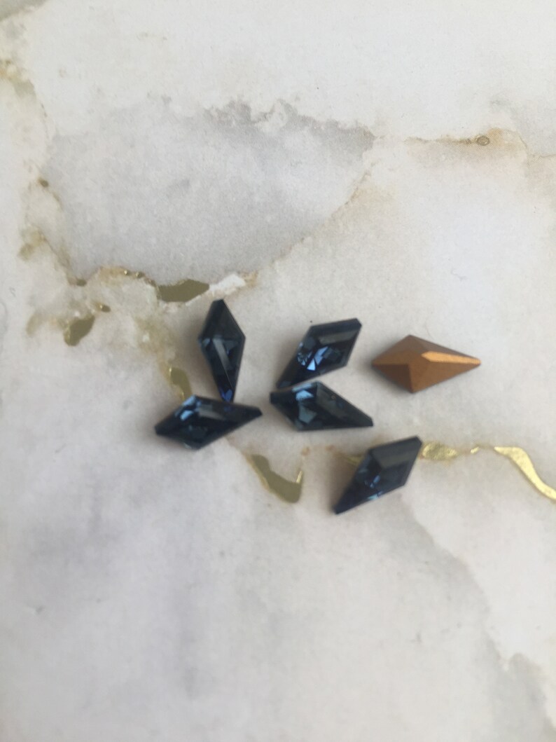 May include: A group of six small, faceted rhinestones. Five are dark blue and one is gold.