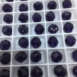 May include: A white plastic tray filled with 25 dark purple glass beads. The beads are arranged in a grid pattern.