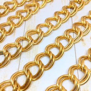Puede incluir: Primer plano de múltiples hilos de eslabones de cadena dorados. Los eslabones son grandes, de forma ovalada y entrelazados, creando un patrón repetitivo. Las cadenas están dispuestas diagonalmente sobre una superficie clara.