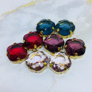 May include: Assortment of eight square-shaped glass rhinestones with gold settings. The rhinestones are in shades of red, pink, purple, and blue.