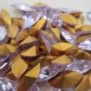 Puede incluir: Un mont&oacute;n de piedras de cristal transparentes, facetadas, ovaladas e iridiscentes con un revestimiento met&aacute;lico dorado en la parte posterior. Las piedras de cristal est&aacute;n esparcidas sobre una superficie blanca.