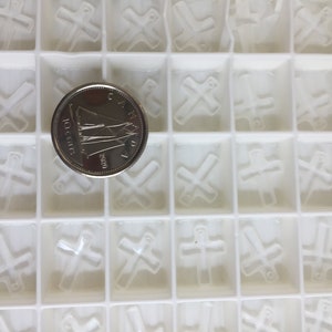 May include: A white plastic mold with 25 individual compartments, each containing a raised cross shape. A Canadian 10-cent coin is placed in the center of the mold.