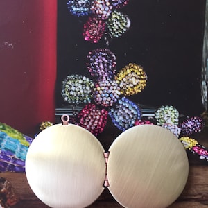 May include: A gold-toned locket with a hinged opening. The locket is round and has a smooth, brushed finish.