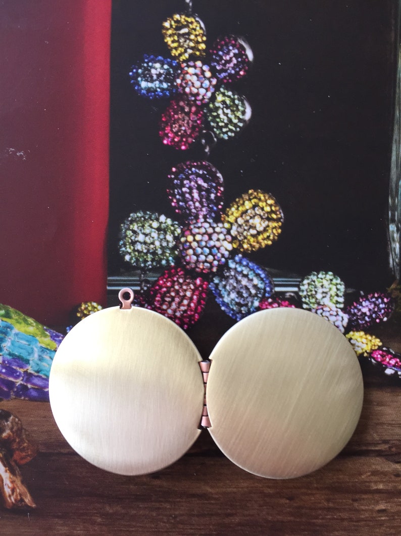 May include: A gold-toned locket with a hinged opening. The locket is round and has a smooth, brushed finish.