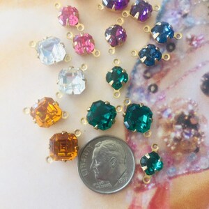 May include: A collection of colorful rhinestone connectors in various shapes and sizes. The gemstones are in shades of purple, pink, blue, green, orange, and clear. Each stone is set in a gold-tone metal setting with loops for attaching to other components.