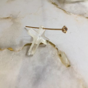 May include: A clear cross pendant with a gold-toned wire and a small clear gemstone at the end.