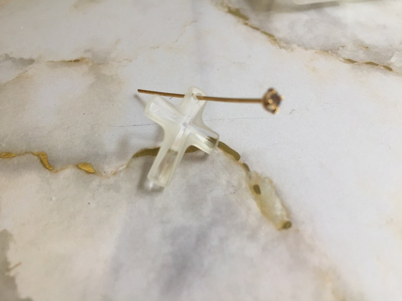 May include: A clear cross pendant with a gold-toned wire and a small clear gemstone at the end.