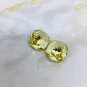 May include: Two square-shaped, faceted, yellow glass rhinestones.