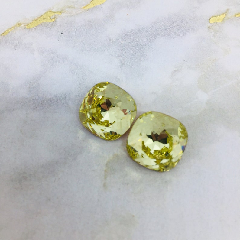 May include: Two square-shaped, faceted, yellow glass rhinestones.