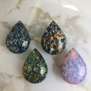 May include: Four teardrop-shaped glass paperweights with a speckled pattern. The paperweights are in shades of blue, green, orange, and pink.