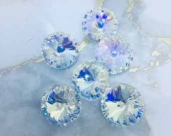 Puede incluir: Un grupo de seis piedras de cristal transparente iridiscente con un diseño facetado. Las piedras están dispuestas en forma de pirámide sobre una superficie de mármol azul claro.