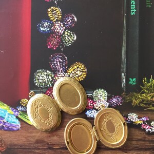 May include: Three gold oval-shaped locket pendants with intricate designs. The lockets are open and show the inside of the locket. The lockets are on a wooden surface.