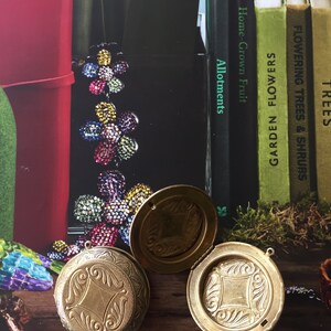 May include: Two gold-coloured, round, hinged pocket watches with ornate designs on the front. The watches are open and lying on a wooden surface.