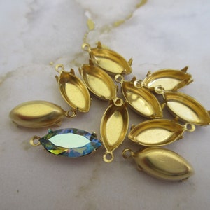 Puede incluir: Un grupo de engastes de metal dorado para piedras de forma marquesa. Los engastes tienen un acabado liso y pulido y est&aacute;n dise&ntilde;ados para sujetar una piedra en su lugar. Un engaste se muestra con una piedra de forma marquesa transparente e iridiscente.