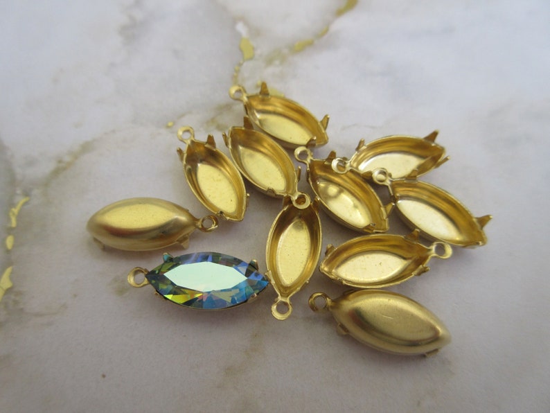 Puede incluir: Un grupo de engastes de metal dorado para piedras de forma marquesa. Los engastes tienen un acabado liso y pulido y est&aacute;n dise&ntilde;ados para sujetar una piedra en su lugar. Un engaste se muestra con una piedra de forma marquesa transparente e iridiscente.