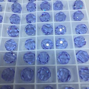May include: A close-up view of a tray of light blue round glass beads. The beads are arranged in a grid pattern and are all the same size.