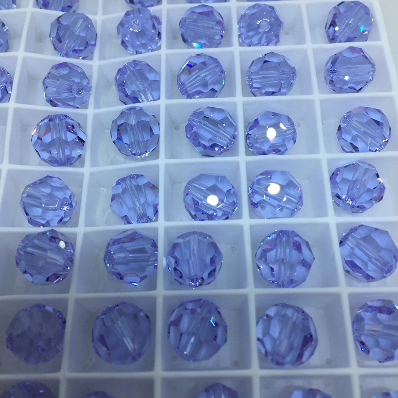May include: A close-up view of a tray of light blue round glass beads. The beads are arranged in a grid pattern and are all the same size.