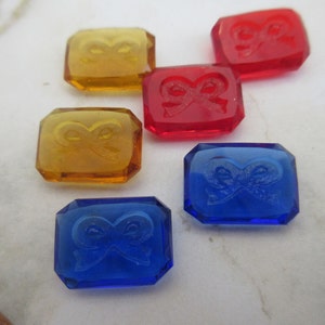 Puede incluir: Cinco azulejos de vidrio con un diseño de lazo. Los azulejos son de color rojo, azul y amarillo.