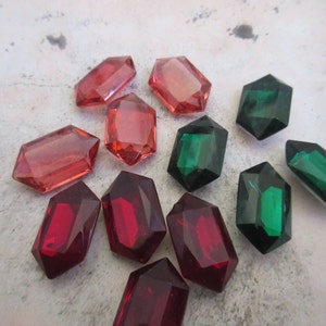 May include: Assortment of faceted glass gems in red, green, and pink. The gems are shaped like octagons and have a shiny, reflective surface.