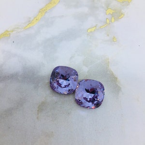 May include: Two light purple square-shaped rhinestones on a white marble background.