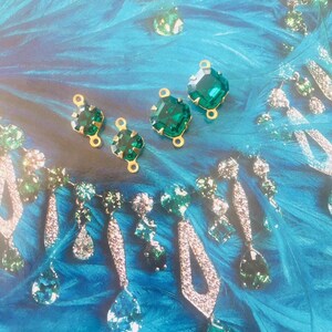 May include: Emerald green gemstone jewelry and components on a blue background. The image features various earrings and loose gemstones with gold settings. The earrings have a mix of clear and green stones. The background has a feathery texture.