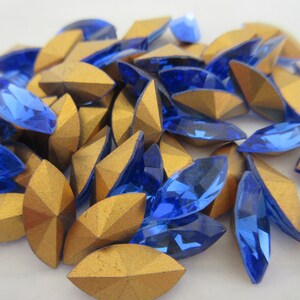 Puede incluir: Un mont&oacute;n de pedrer&iacute;a de cristal azul y dorada. La pedrer&iacute;a tiene forma de marquesa y un dise&ntilde;o facetado.